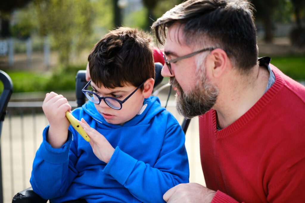 Disabled child on wheelchair using a mobile phone with his father.