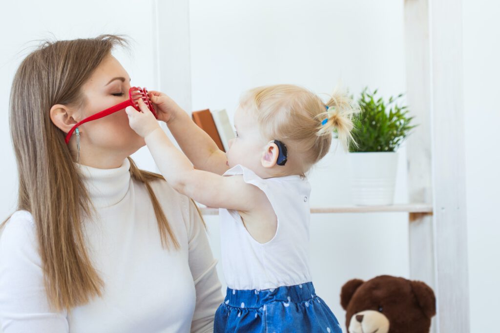 Hearing aid in baby girl's ear. Toddler child wearing a hearing aid at home. Disabled child