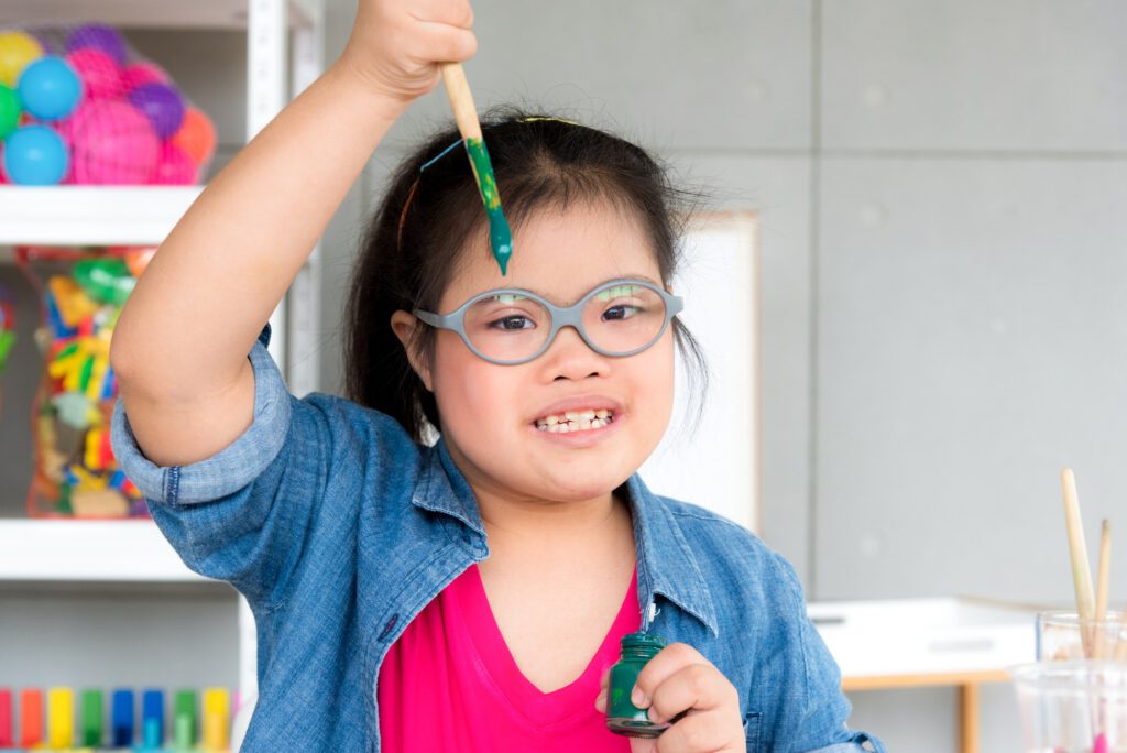 Young autism disabled child complex genetic disorders kid drawing a picture by watercolor.